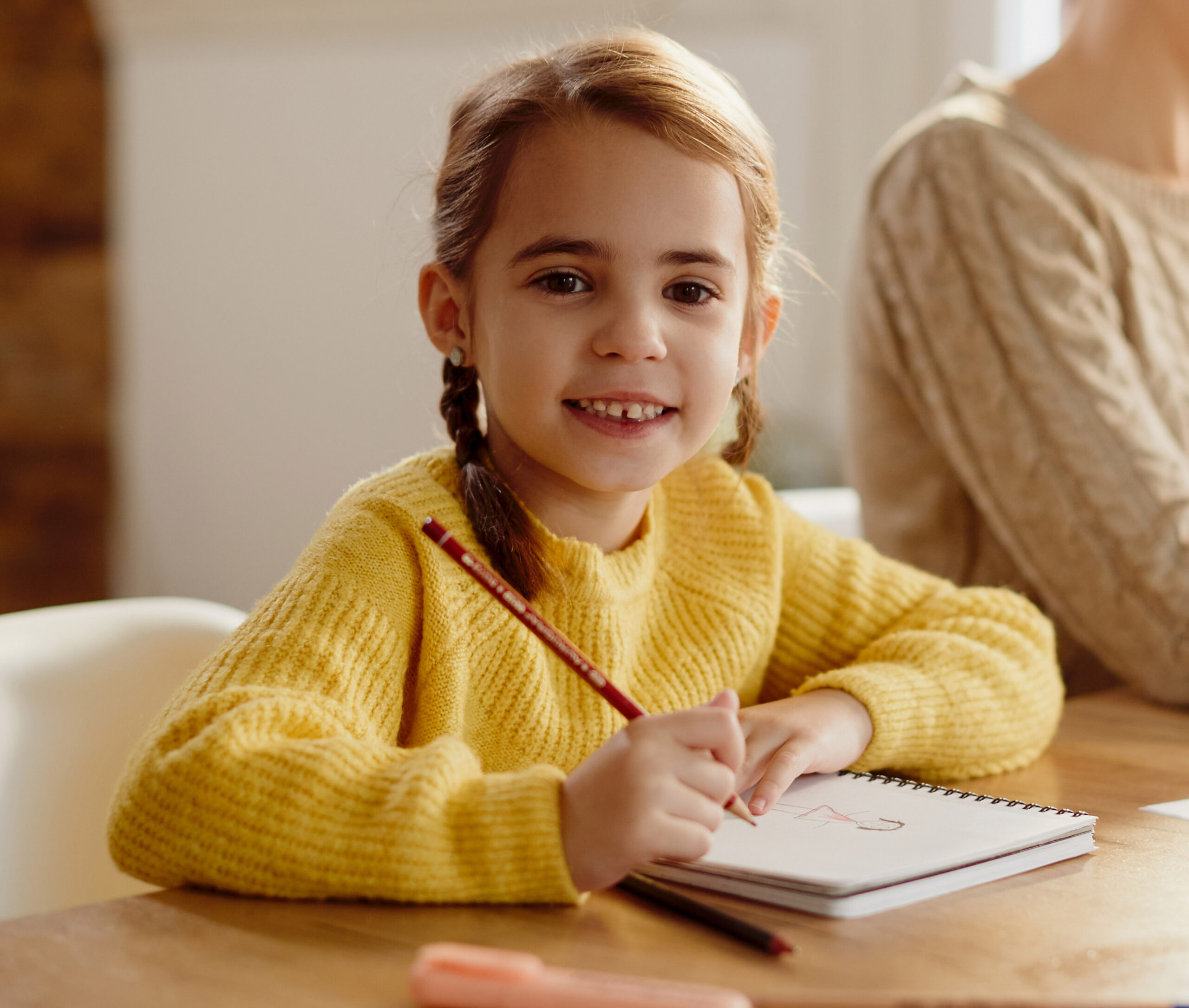 Happy little girl drawing while her mother is working on laptop